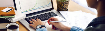 stylish young hipster girl working economist financial analytics holding pen on craft background with laptop and papers