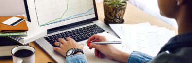 stylish young hipster girl working economist financial analytics holding pen on craft background with laptop and papers